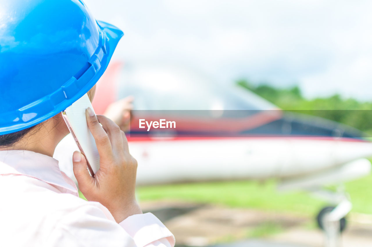 Rear view of mechanic talking on phone while pointing at airplane