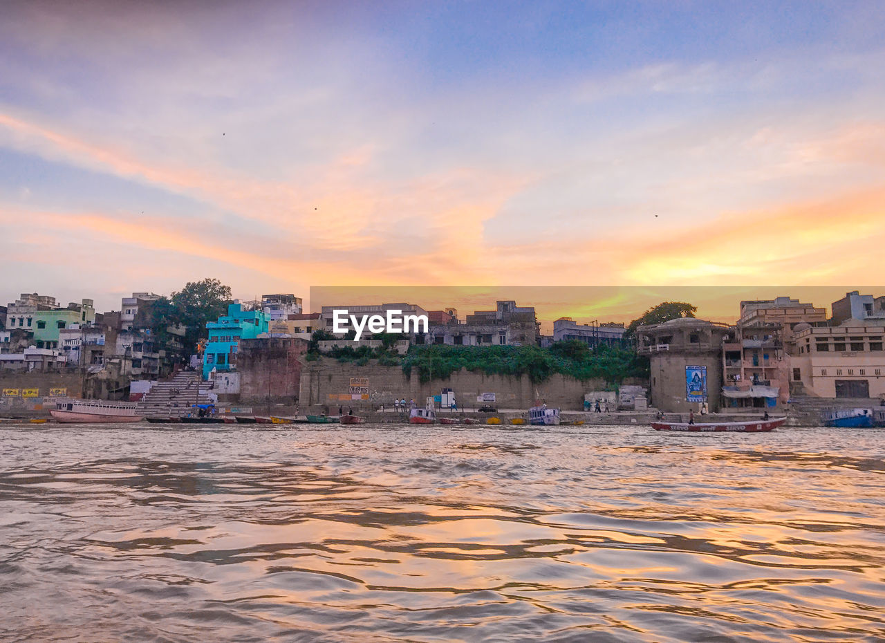 Buildings by sea against sky during sunset