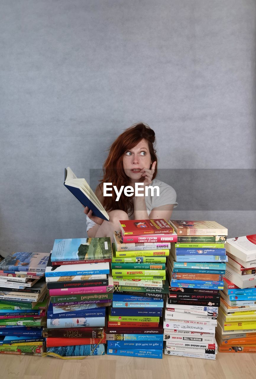 PORTRAIT OF YOUNG WOMAN SITTING ON BOOK WITH BOOKS