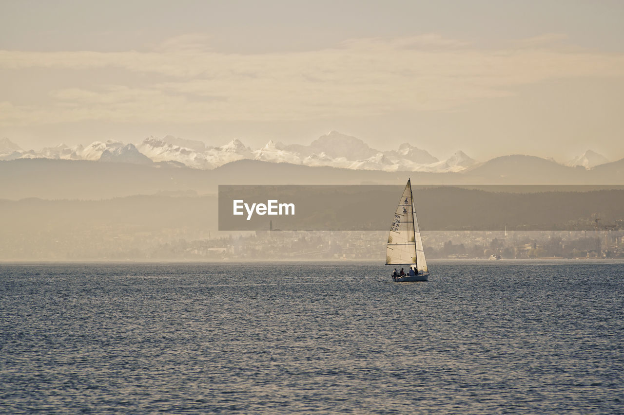 SAILBOAT SAILING IN SEA AGAINST MOUNTAINS