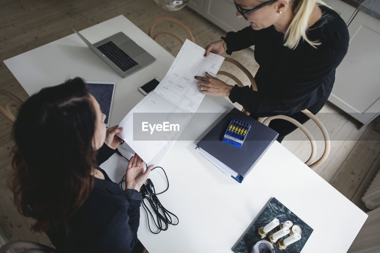 High angle view of female engineers discussing over blueprint at table in home office