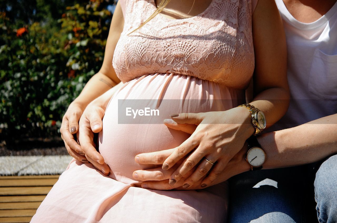 Midsection of pregnant woman with man sitting outdoors