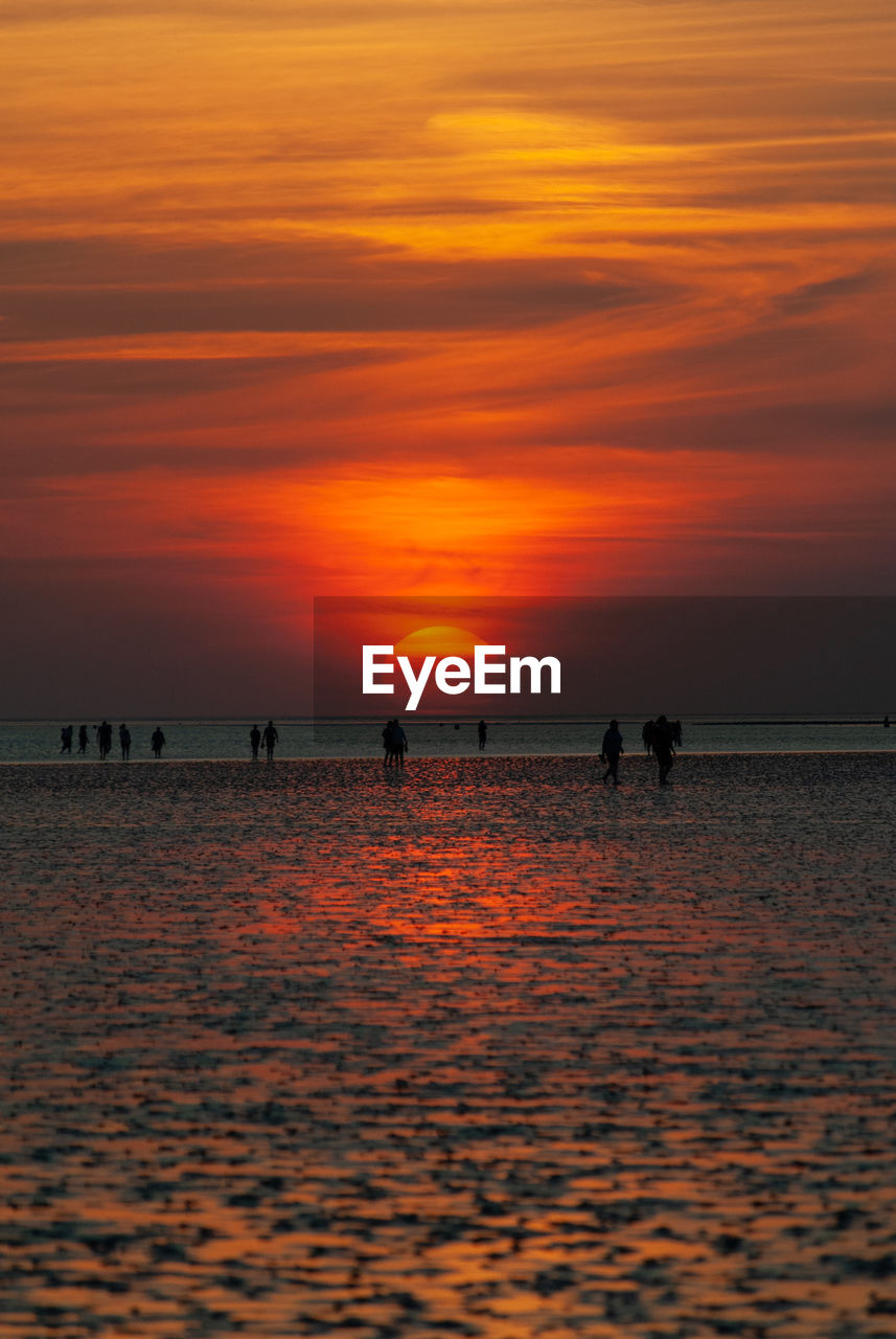 Silhouette people on beach against orange sky