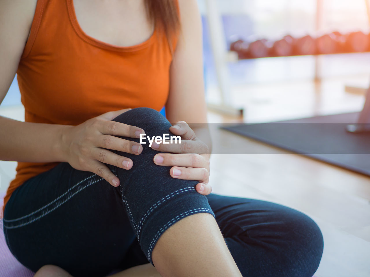 Midsection of woman holding knee while sitting in gym