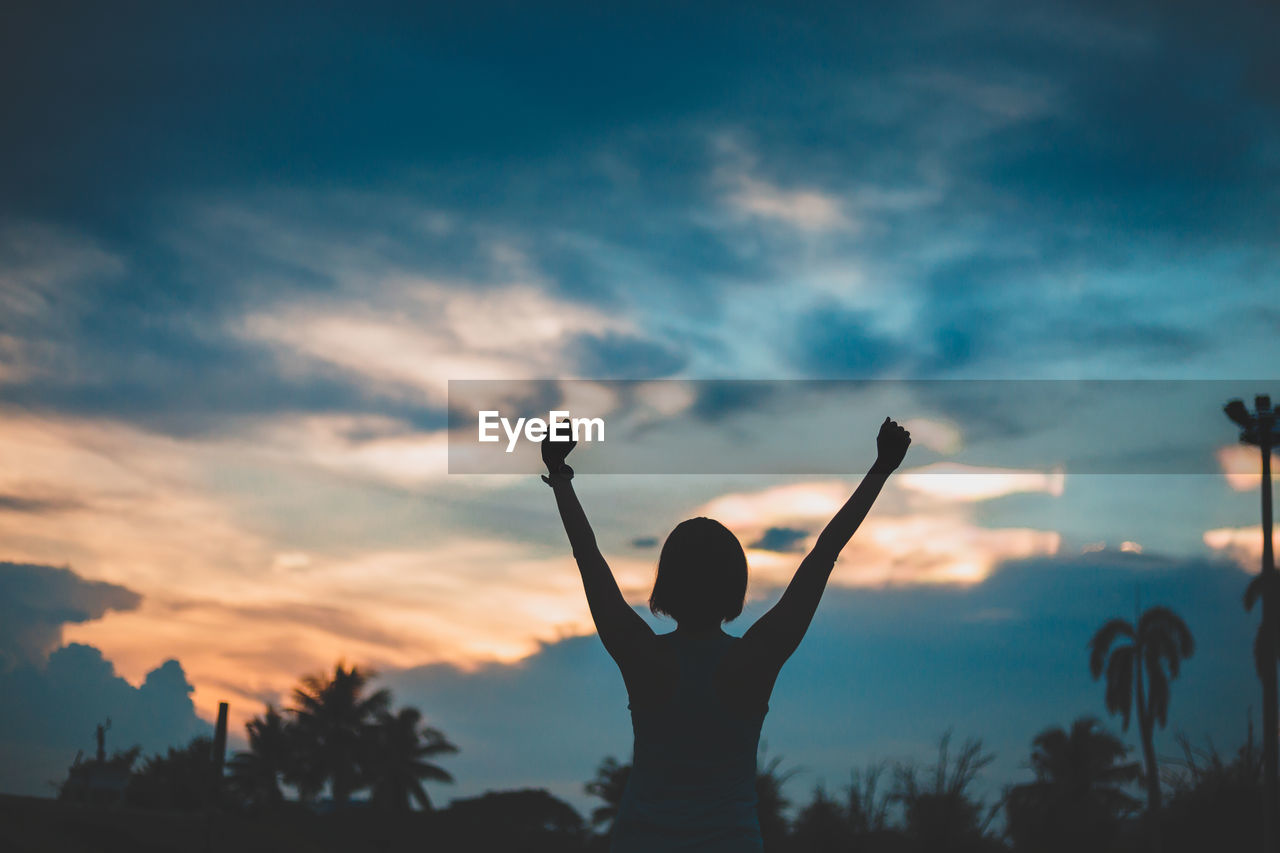 Silhouette woman with arms raised standing against sky during sunset