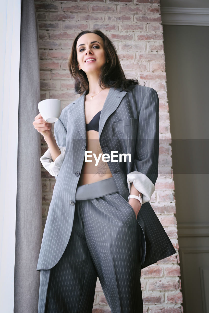 adult, one person, women, business, formal wear, coffee, cup, outerwear, mug, young adult, clothing, coffee cup, businesswoman, standing, drink, portrait, sleeve, indoors, food and drink, female, fashion, brown hair, corporate business, photo shoot, holding, looking, business finance and industry, dress, smiling, hairstyle, refreshment, long hair, lifestyles, three quarter length, happiness, coffee break, front view, emotion, person, looking at camera, blazer, collar, white-collar worker, architecture, human leg, elegance, limb, hot drink, drinking, contemplation, office, enjoyment, jacket