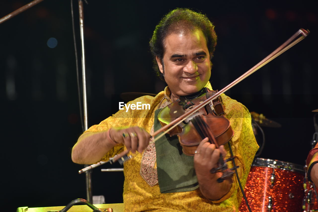 Smiling man playing violin while sitting on stage