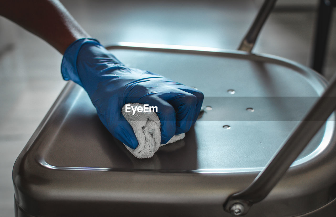 Closeup of the hand of a black woman wearing blue gloves and cleaning a chair. covid 19 prevention. 