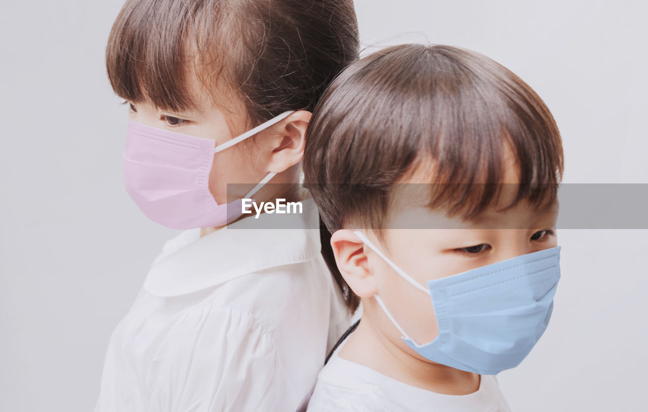 Close-up of siblings wearing masks against white background