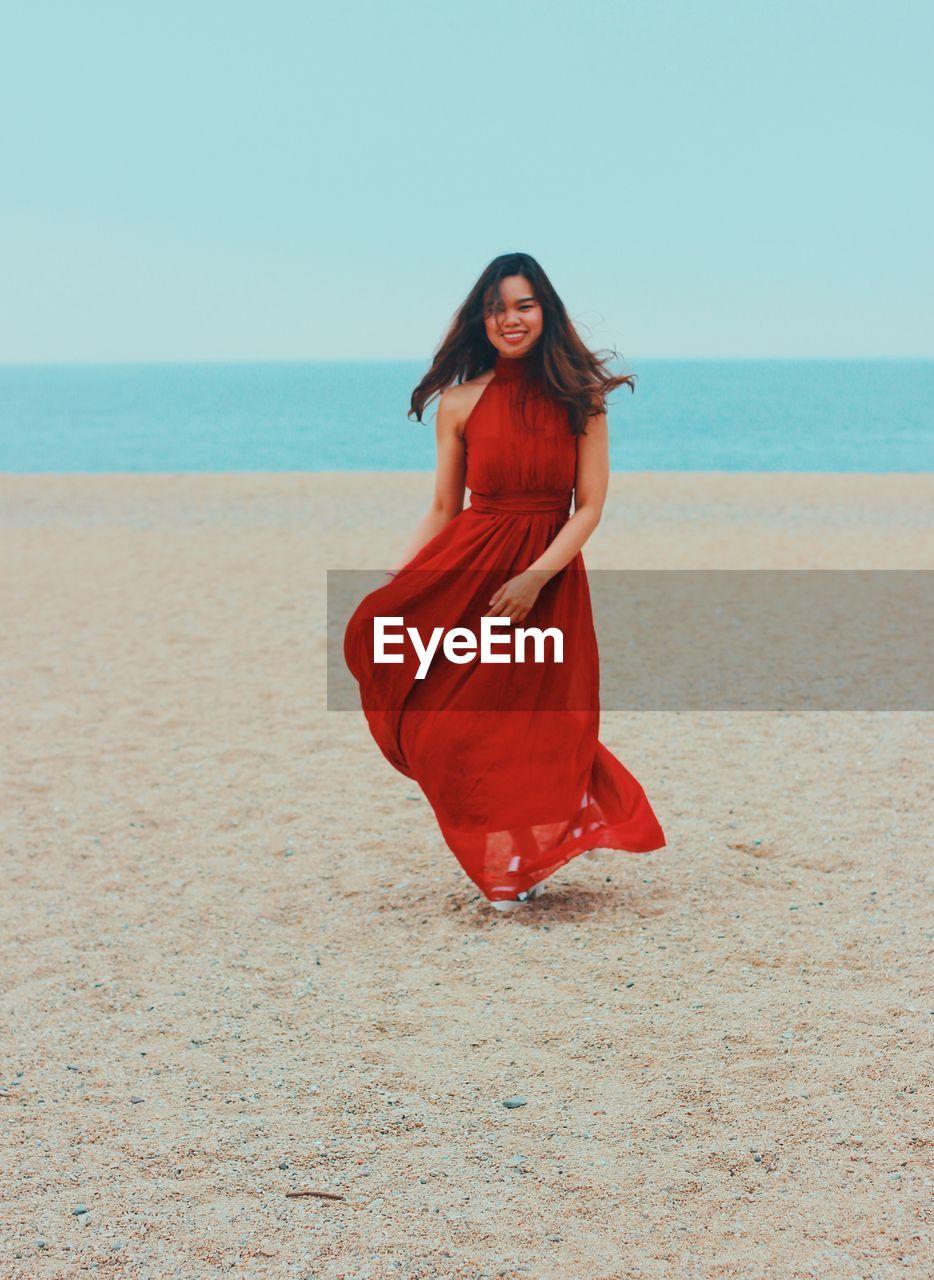 Smiling woman standing on beach against sky