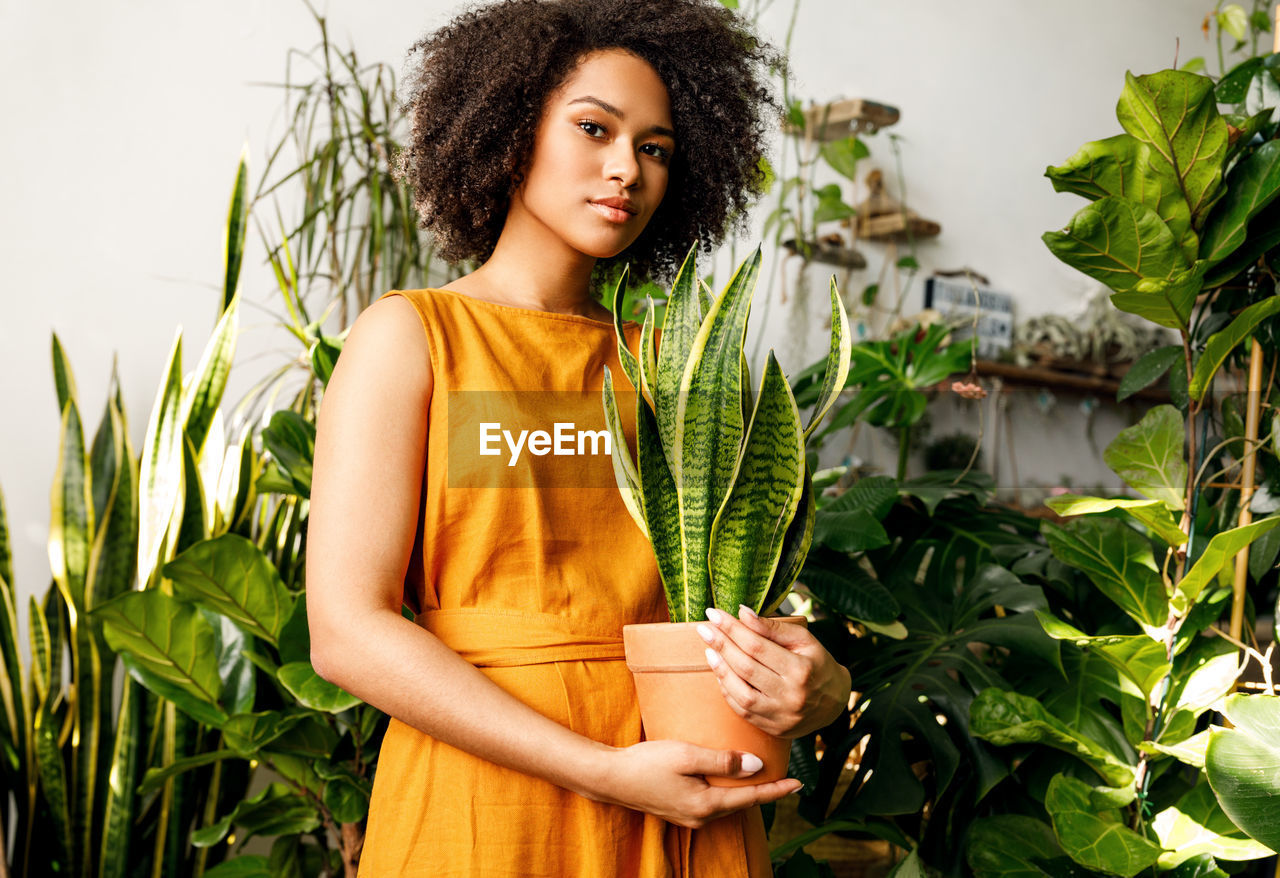 Portrait of teenage girl holding potted plant amid plants