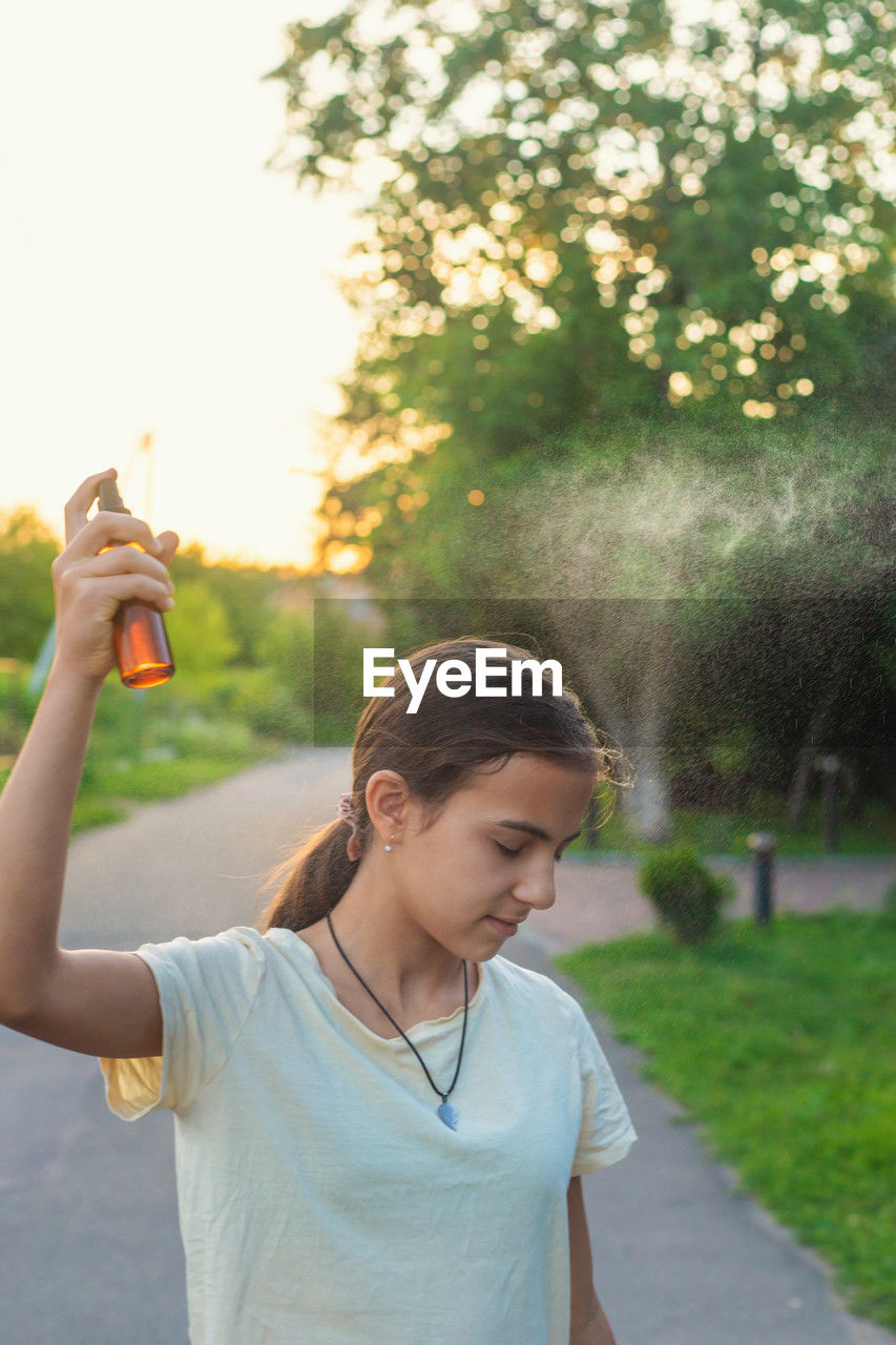 young woman drinking water while standing on road against trees