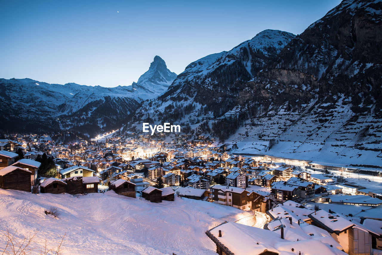 Scenic view of snowcapped mountains by townscape against clear sky during winter