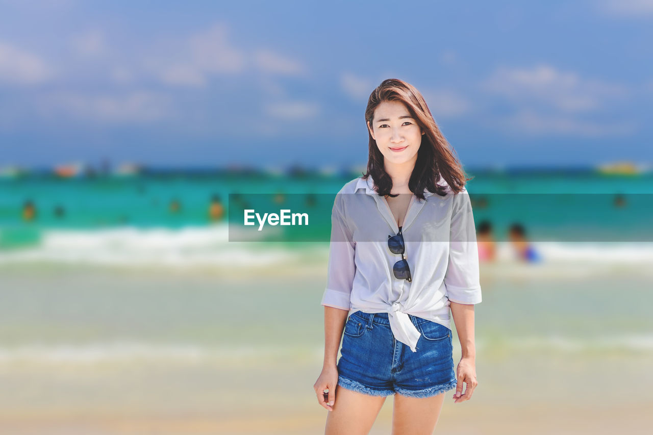 PORTRAIT OF YOUNG WOMAN STANDING AT BEACH