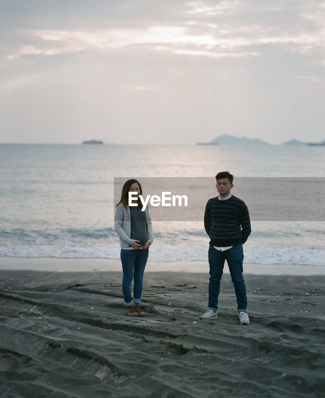 Full length of man and woman standing on beach against sky