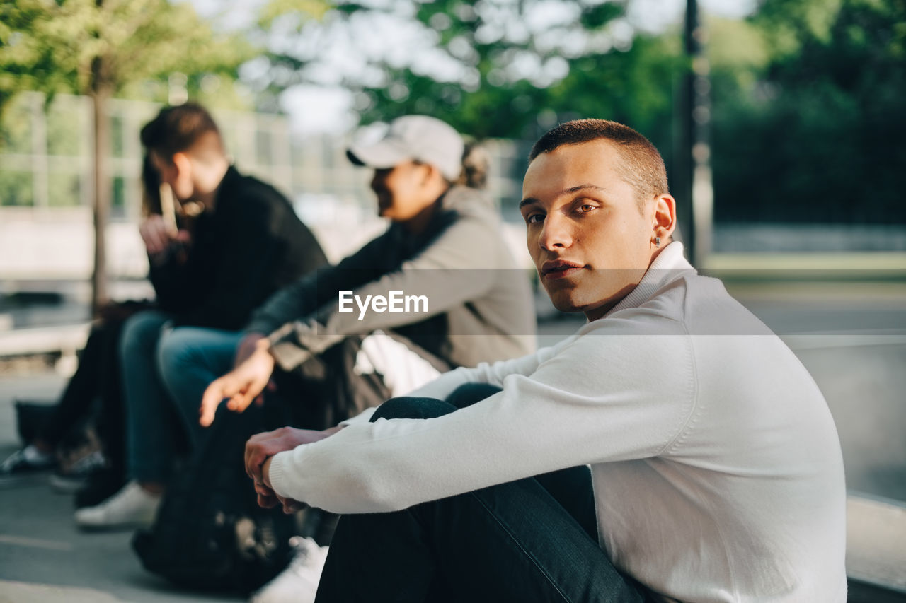 Portrait of young man sitting with friends at park