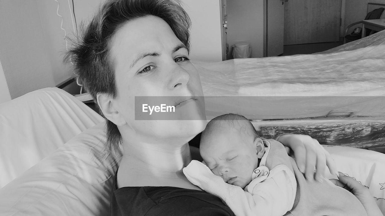 Mother holding newborn while lying on bed at hospital