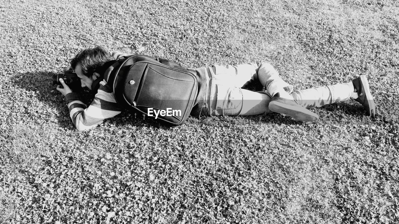 High angle view of man lying while photographing with camera on field