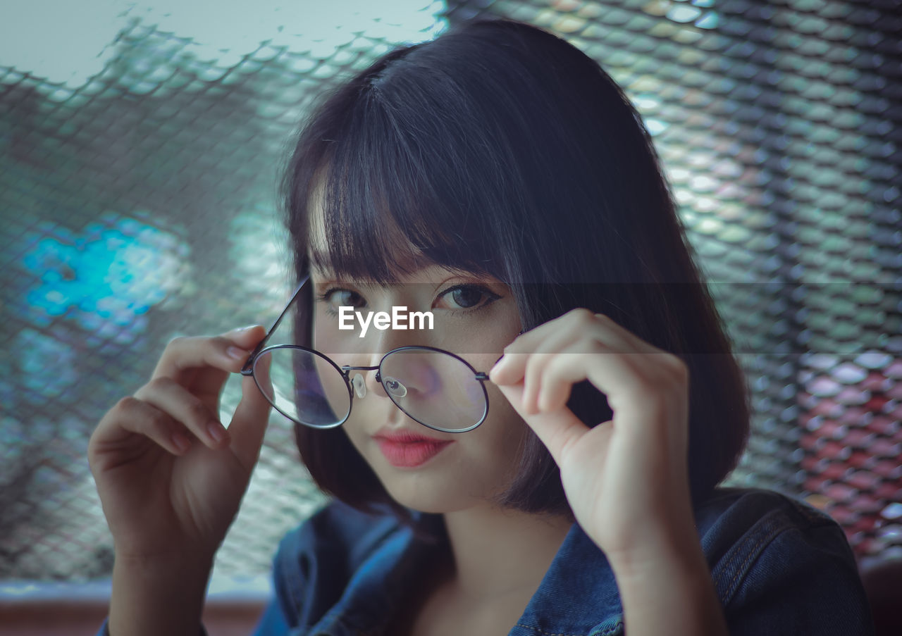 Close-up portrait of young woman wearing eyeglasses against window