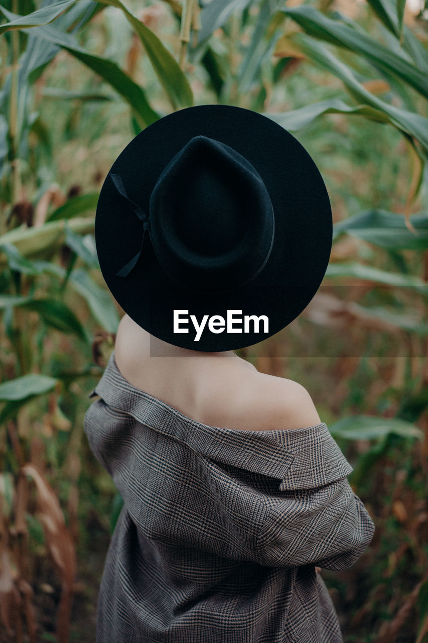 Rear view of woman wearing hat standing amidst plants