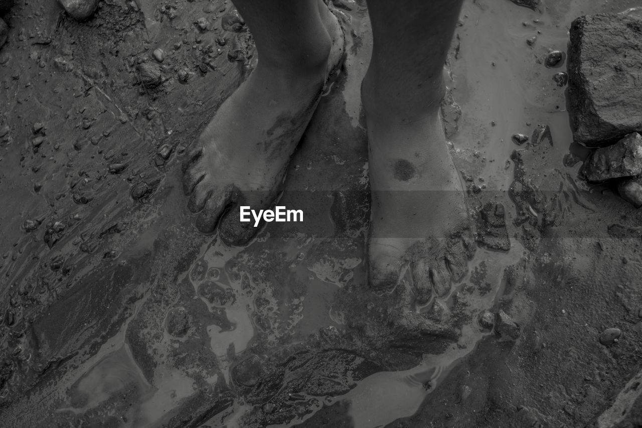 low section, black and white, human leg, black, monochrome, monochrome photography, high angle view, sand, one person, white, darkness, land, soil, shoe, human foot, limb, dirt, human limb, nature, day, beach, lifestyles, standing, outdoors, barefoot, mud, footprint, water, leisure activity, wet
