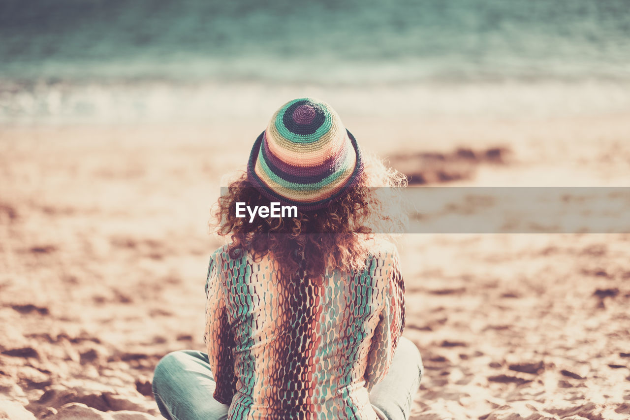 Rear view of woman sitting on beach against sky