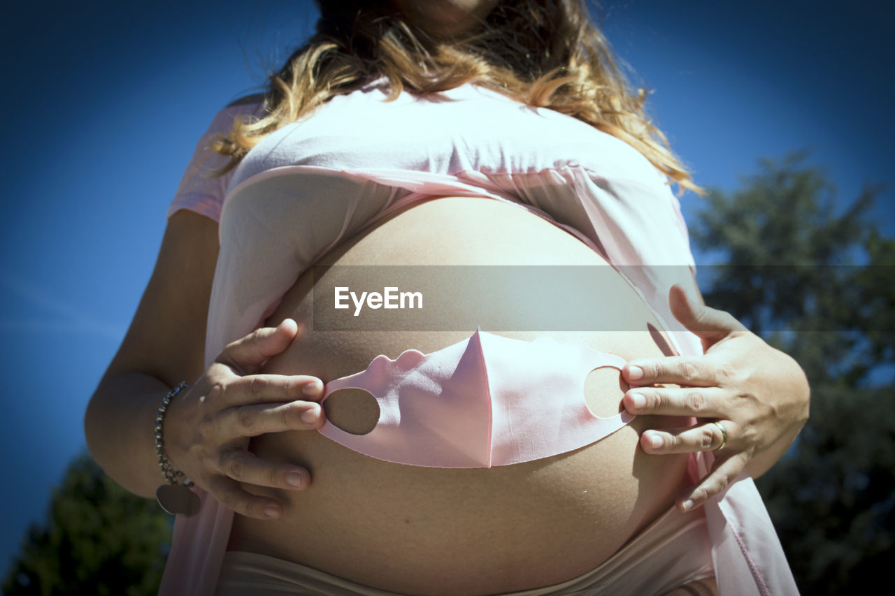 Seven months pregnant woman with baby mask over her gut. pink color