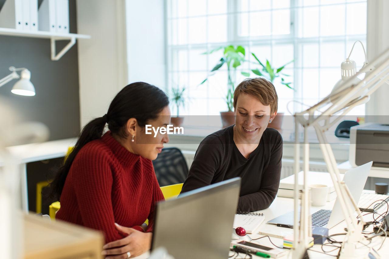 Smiling multi-ethnic female professionals working at illuminated desk in creative office