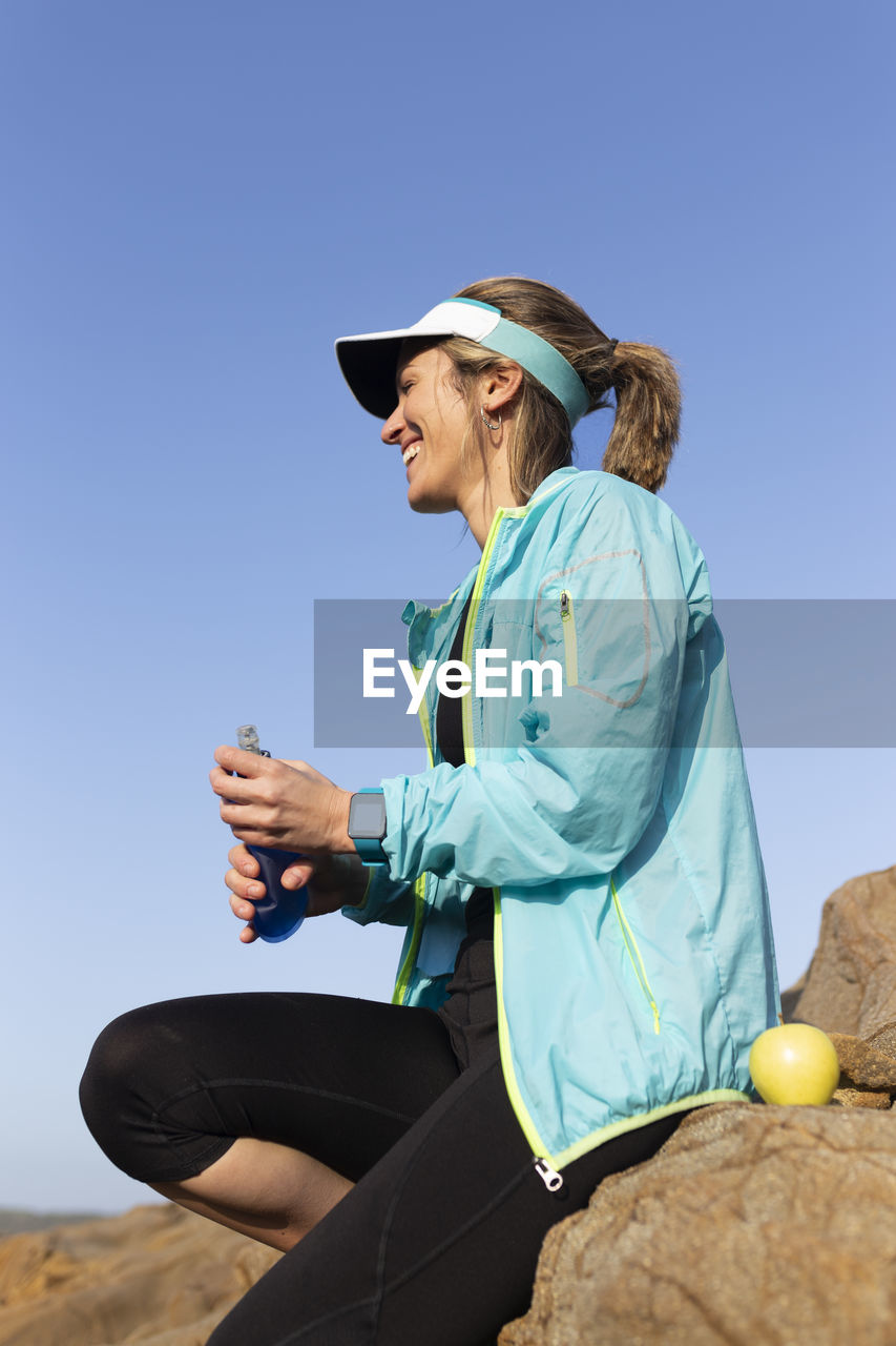 Happy woman with water bottle sitting on rock