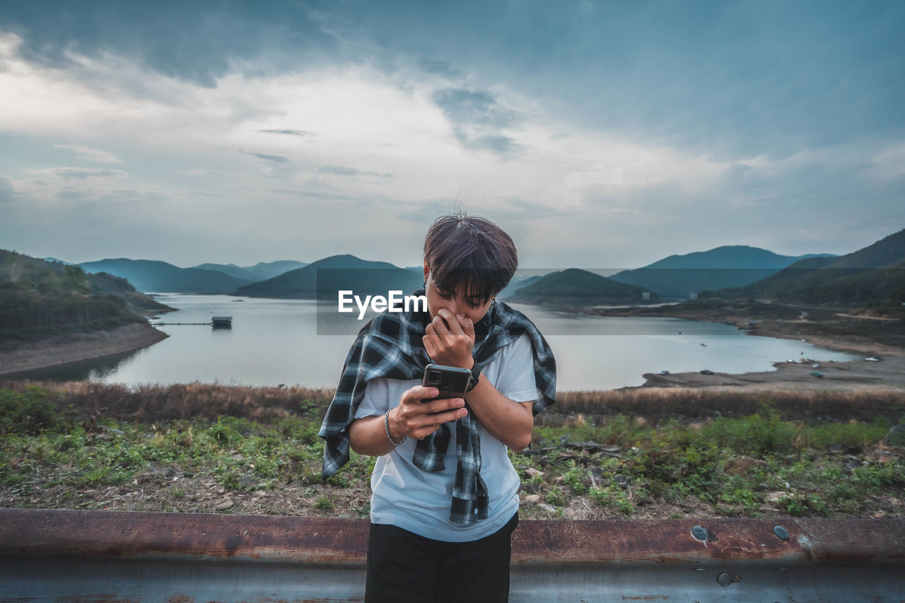 MAN PHOTOGRAPHING WHILE USING MOBILE PHONE AGAINST SKY