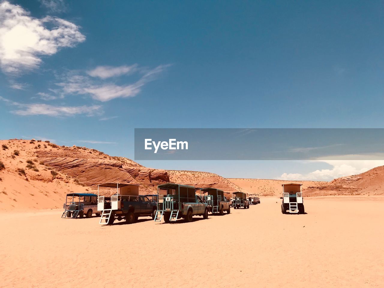 Vehicles on sand against blue sky at desert