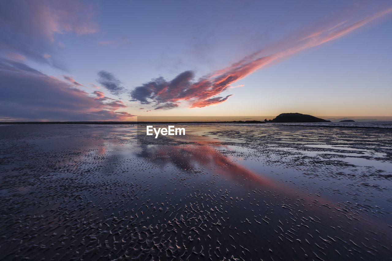 Scenic view of beach against sky at sunset