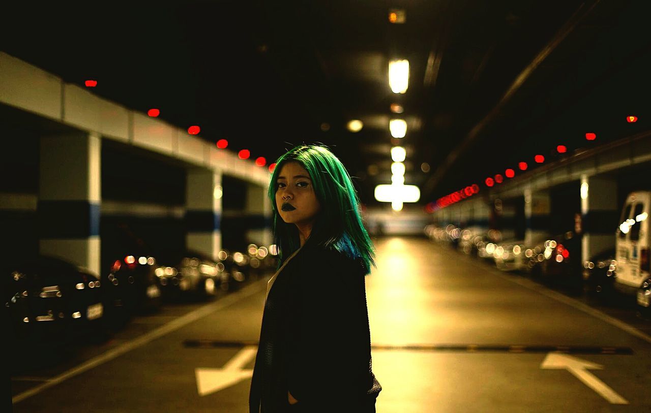 Portrait of woman with dyed hair standing in illuminated basement