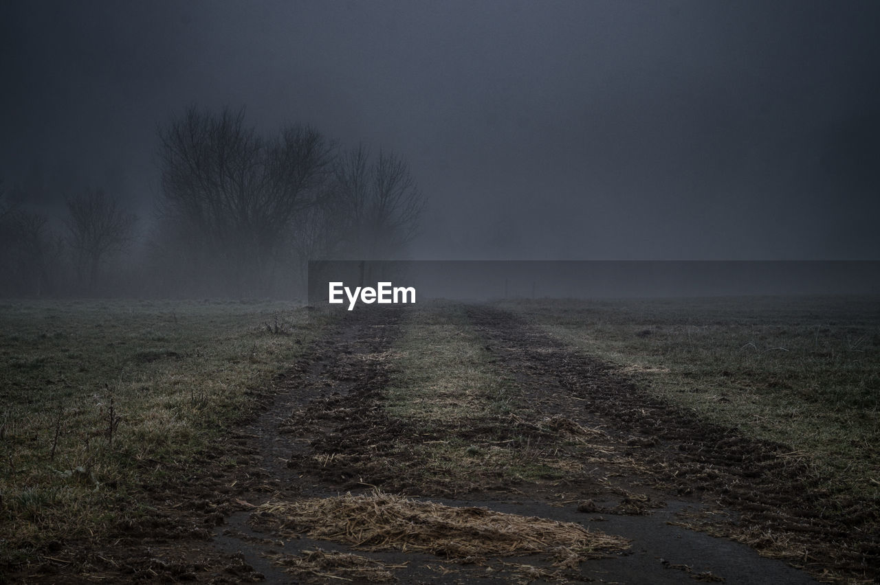 Empty dirt road against sky during foggy weather