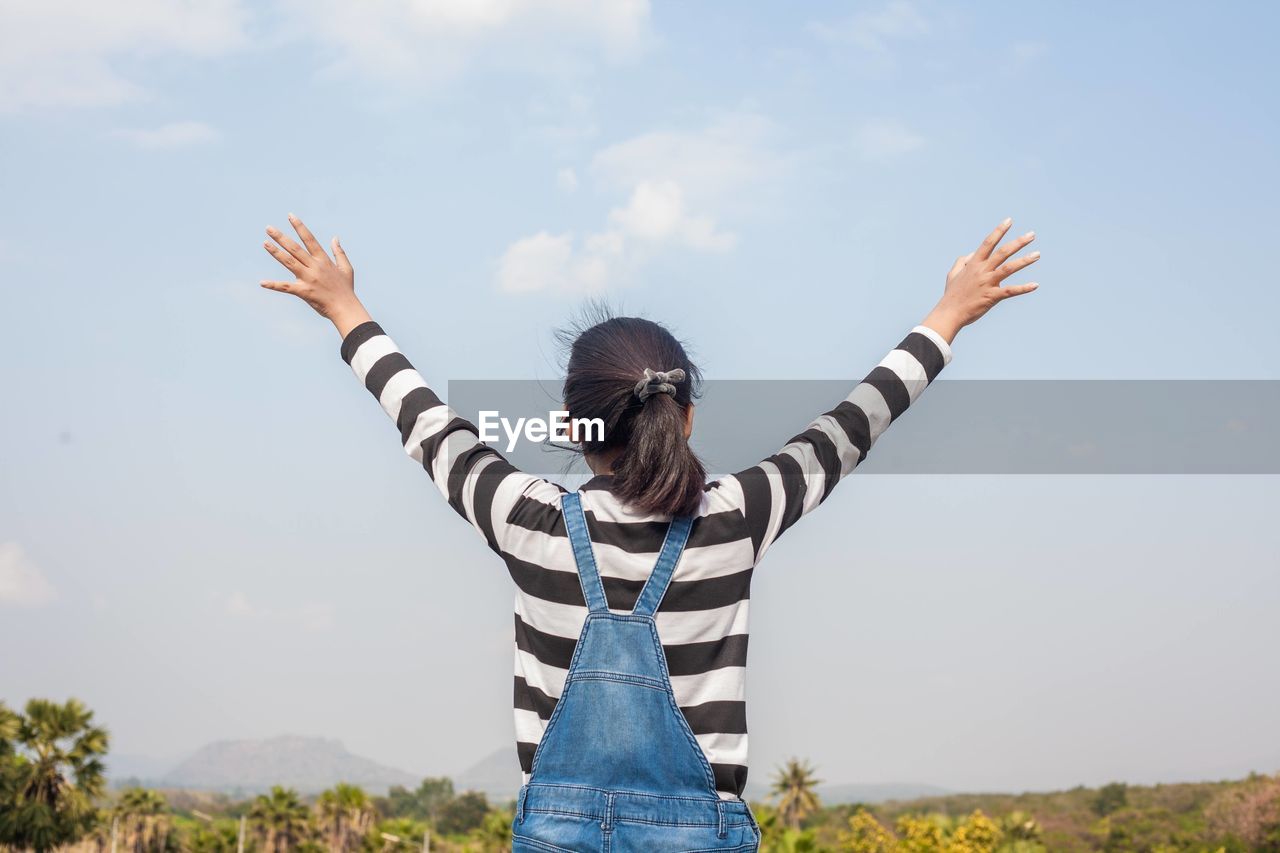 Rear view of woman with arms raised against sky