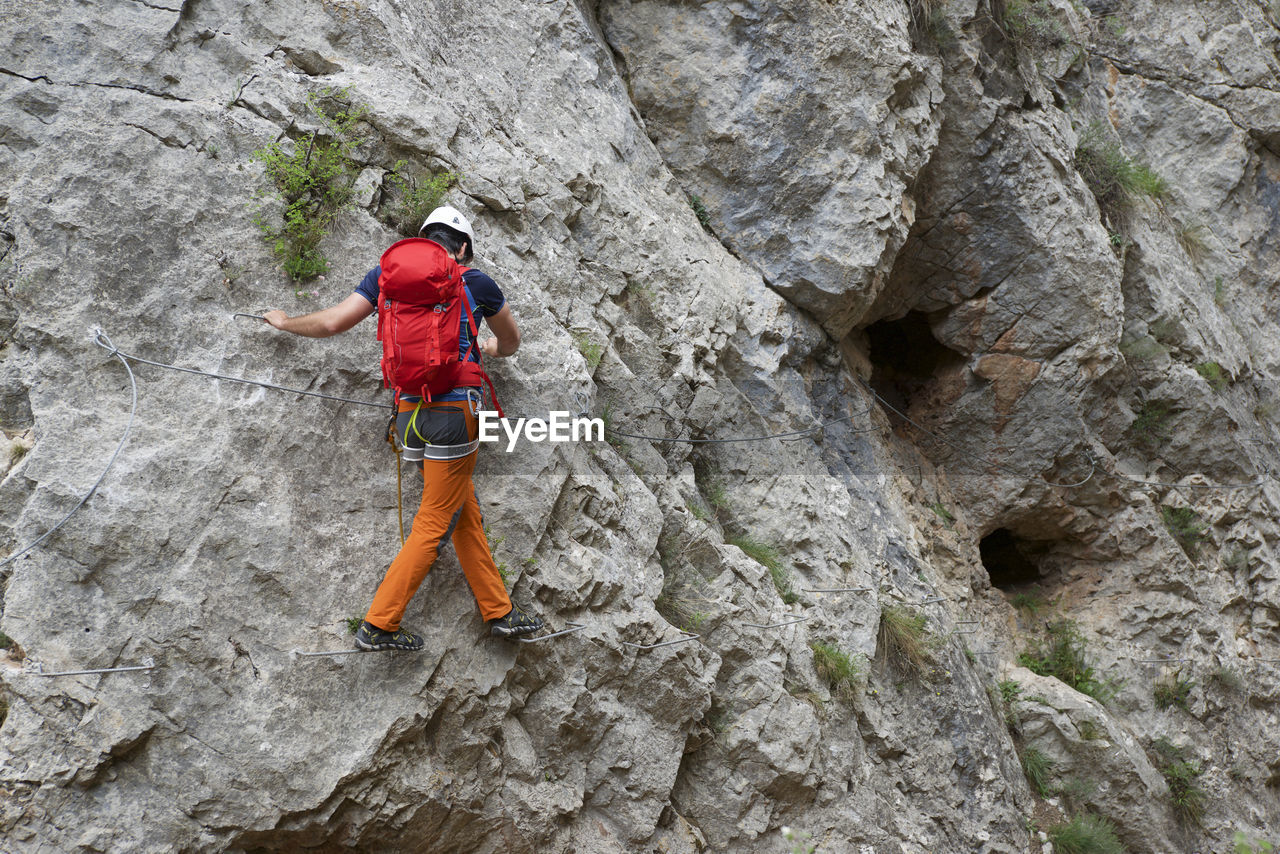 Full length of backpacker walking on metal mounted on rock formation