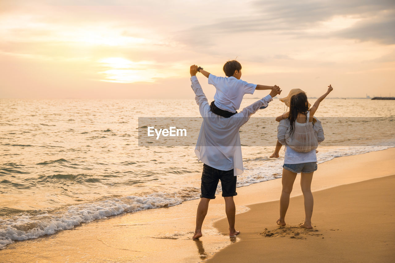 side view of woman standing at beach against sky during sunset