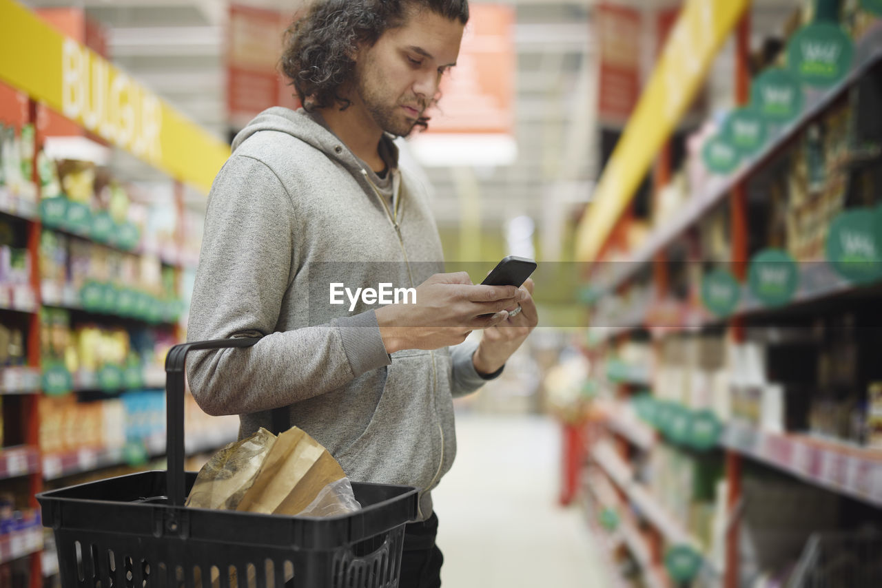 Man in supermarket comparing prices during inflation on cell phone