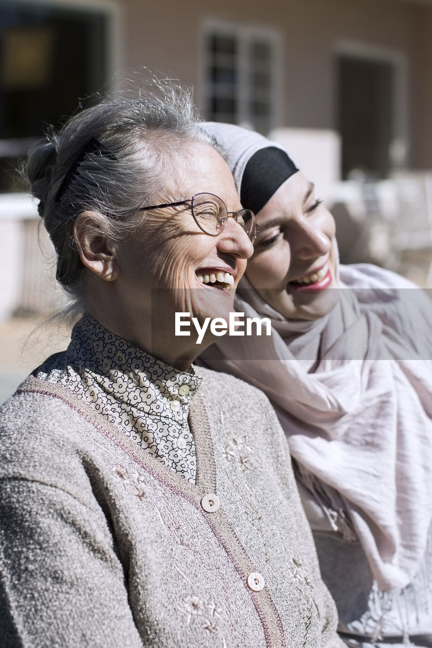 Smiling senior woman and female home caregiver in front of house