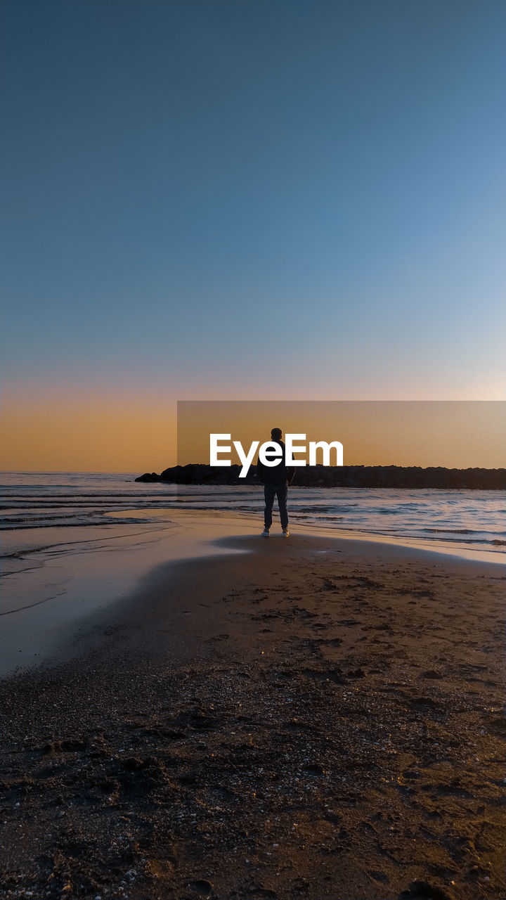 Silhouette person standing on beach against sky during sunset