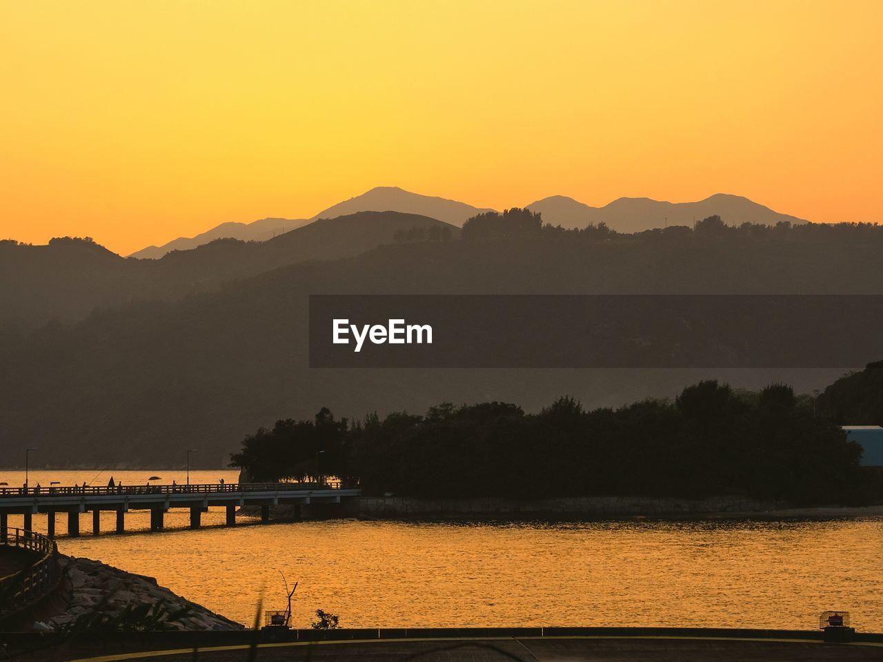 Scenic view of river and silhouette mountains against orange sky