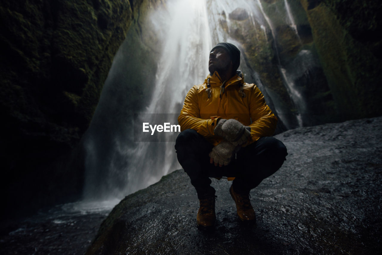 Full length of man crouching against waterfall in cave