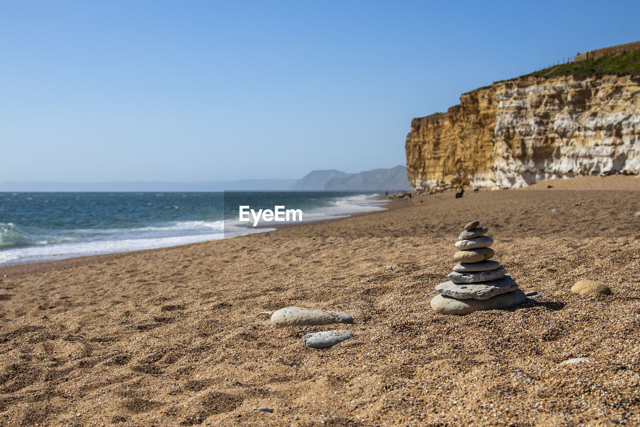 land, beach, sea, sky, water, sand, nature, coast, clear sky, shore, rock, body of water, scenics - nature, ocean, beauty in nature, horizon over water, travel destinations, tranquility, coastline, cliff, wave, horizon, day, no people, tranquil scene, terrain, sunny, travel, blue, outdoors, vacation, motion, holiday, sunlight, tourism, trip, non-urban scene, idyllic