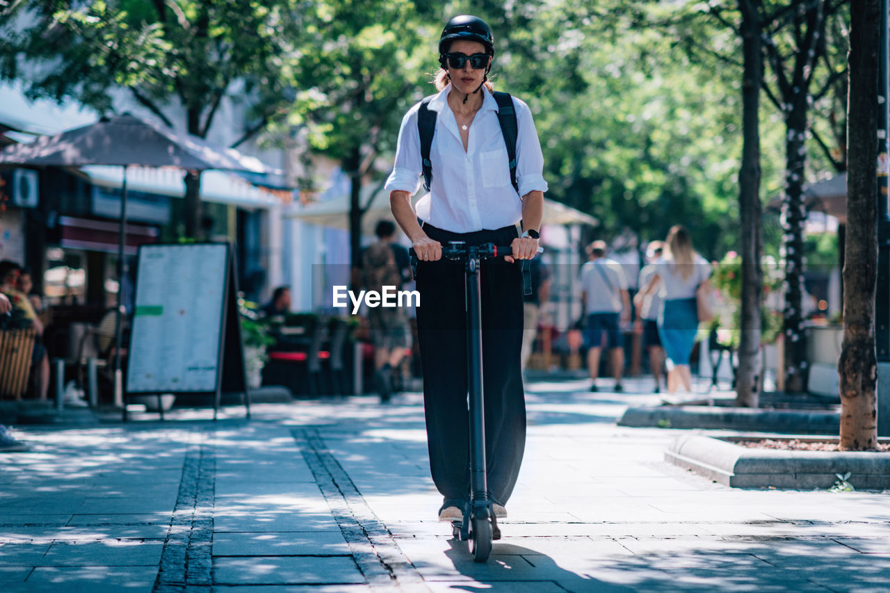 Full length of woman riding electric push scooter on walkway