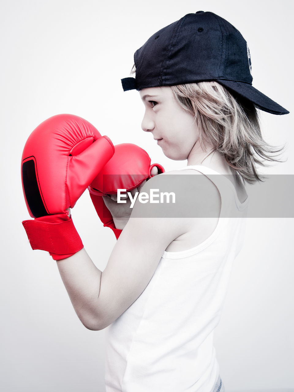 Side view of boy wearing boxing gloves while standing against white background