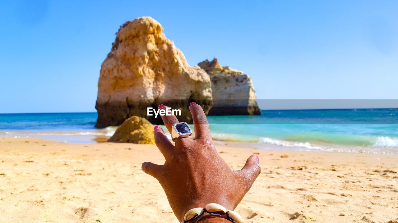 Cropped hand of mid adult woman gesturing at beach against clear sky during sunny day