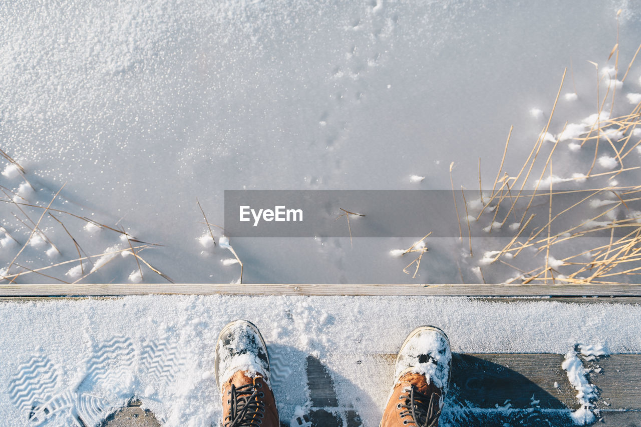 Low section of man standing on pier over frozen lake during winter