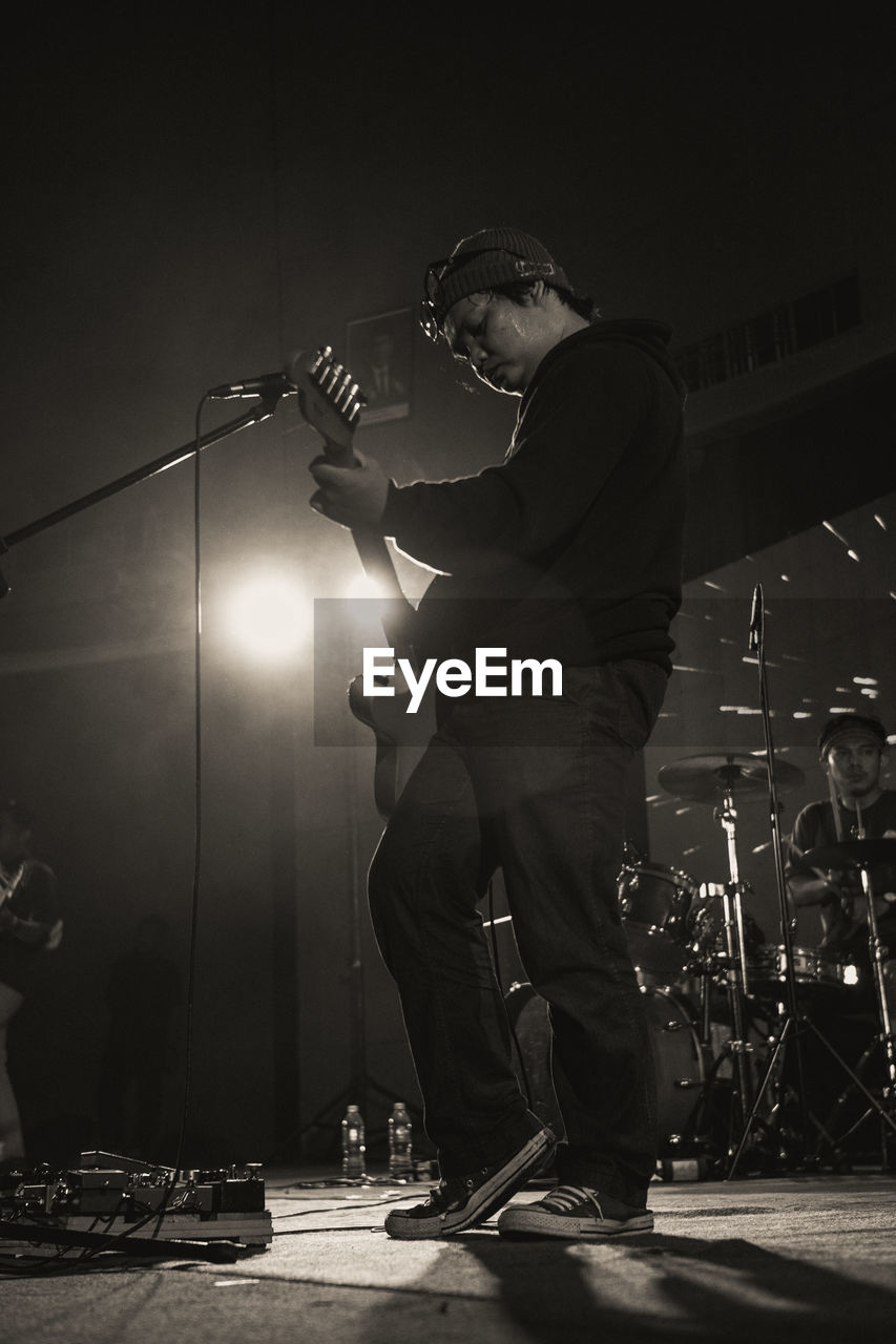 black, black and white, arts culture and entertainment, music, performance, musician, monochrome, musical instrument, adult, men, input device, microphone, monochrome photography, stage, one person, skill, rock music, concert, entertainment, event, guitar, performance art, full length, darkness, performing arts event, standing, musical equipment, performing arts, white, night, popular music concert, enjoyment, string instrument, young adult, lighting equipment, nightlife, singing, plucking an instrument, electric guitar, occupation, drummer, back lit, light, crowd, singer, illuminated