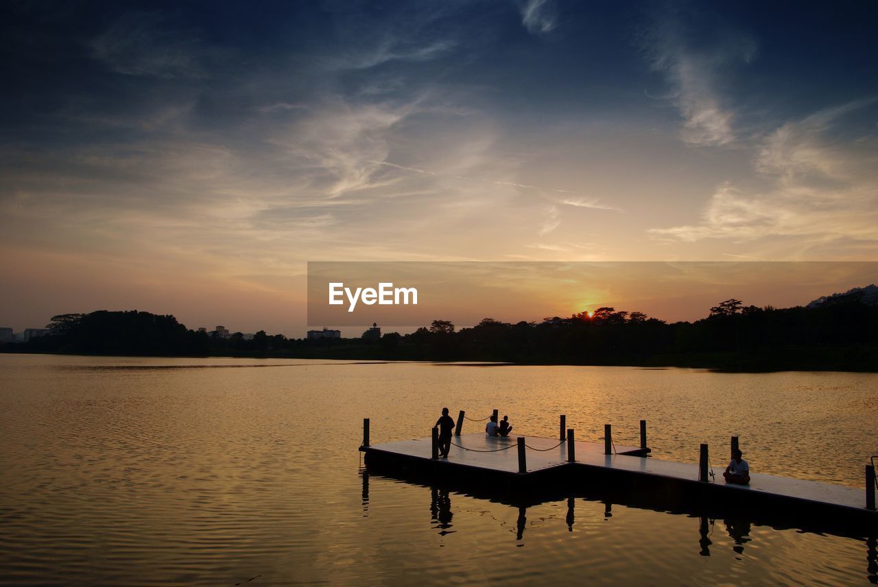 Silhouette people on pier in lake at sunset