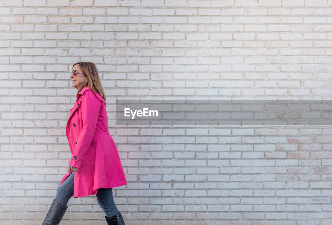 Side view of woman walking by brick wall